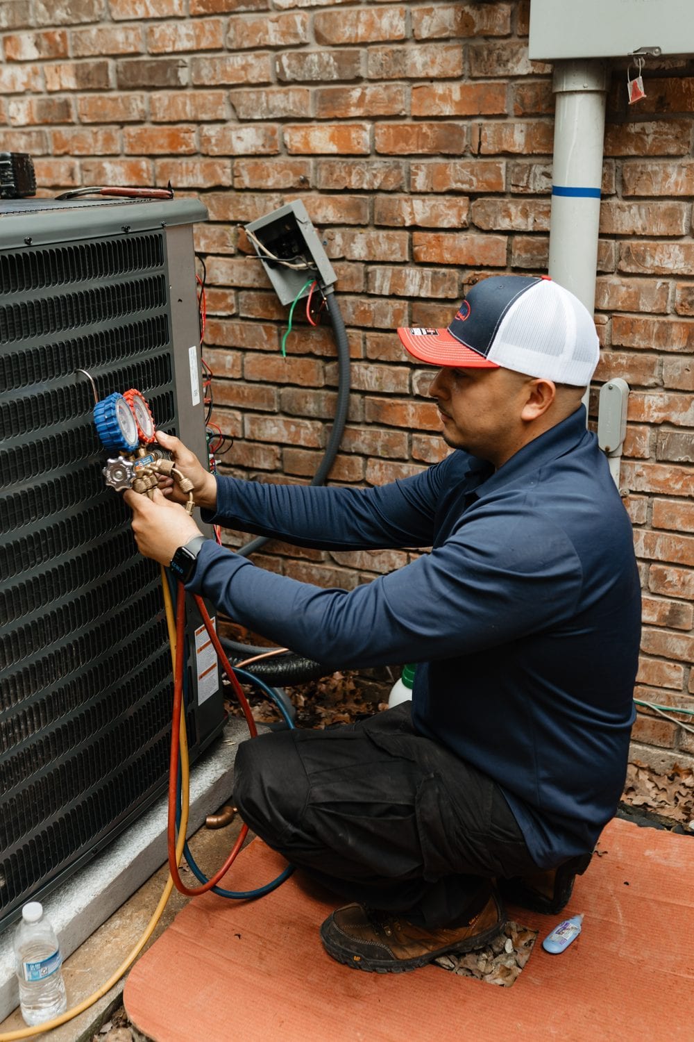 A Lexany's Heating & AC technician checking an outdoor AC system's refrigerant with gauges during a seasonal tune-up in Forney, TX