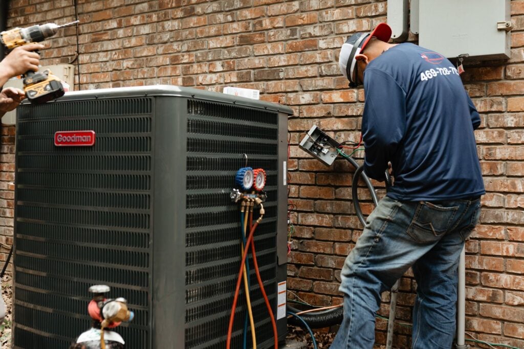 Lexany's Heating & AC technician wiring a Goodman outdoor unit with refrigerant gauges attached